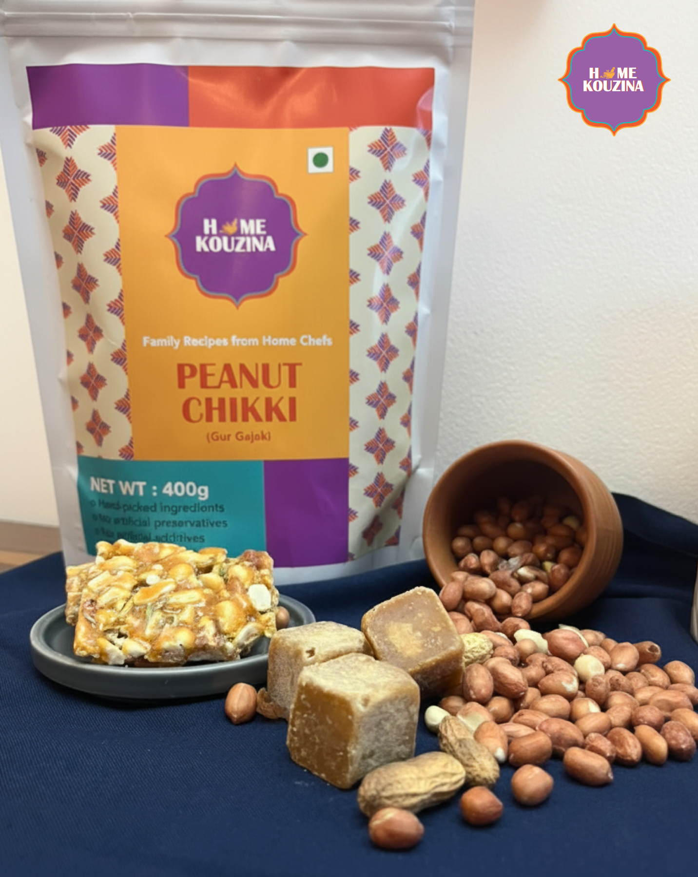 Peanut Chikki with packaging and peanuts on a blue surface, featuring Home Kuzina brand.