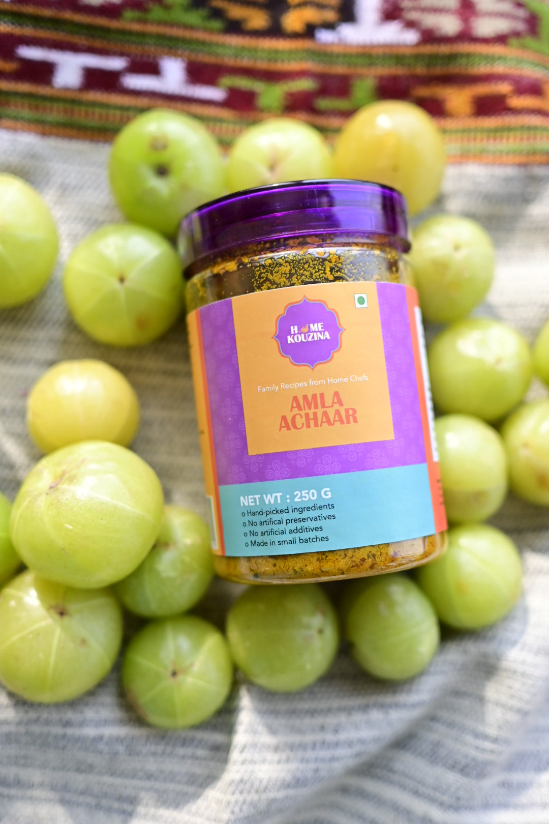 Jar of amla pickle surrounded by green amla fruits on a textured fabric background
