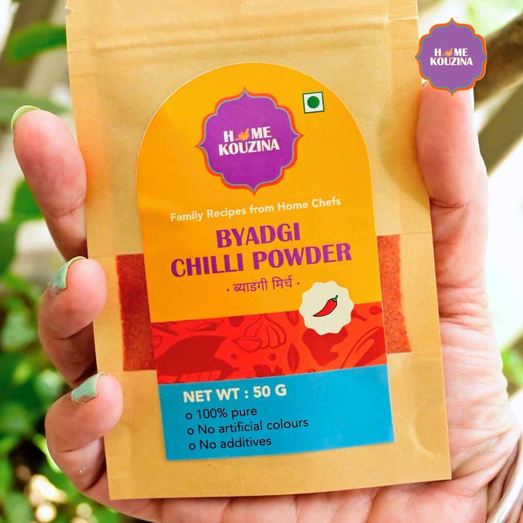 Hand holding Home Kouzina Byadgi Chilli Powder 50g pouch outdoors – small-batch, preservative-free Byadgi chilli powder for authentic Indian cooking