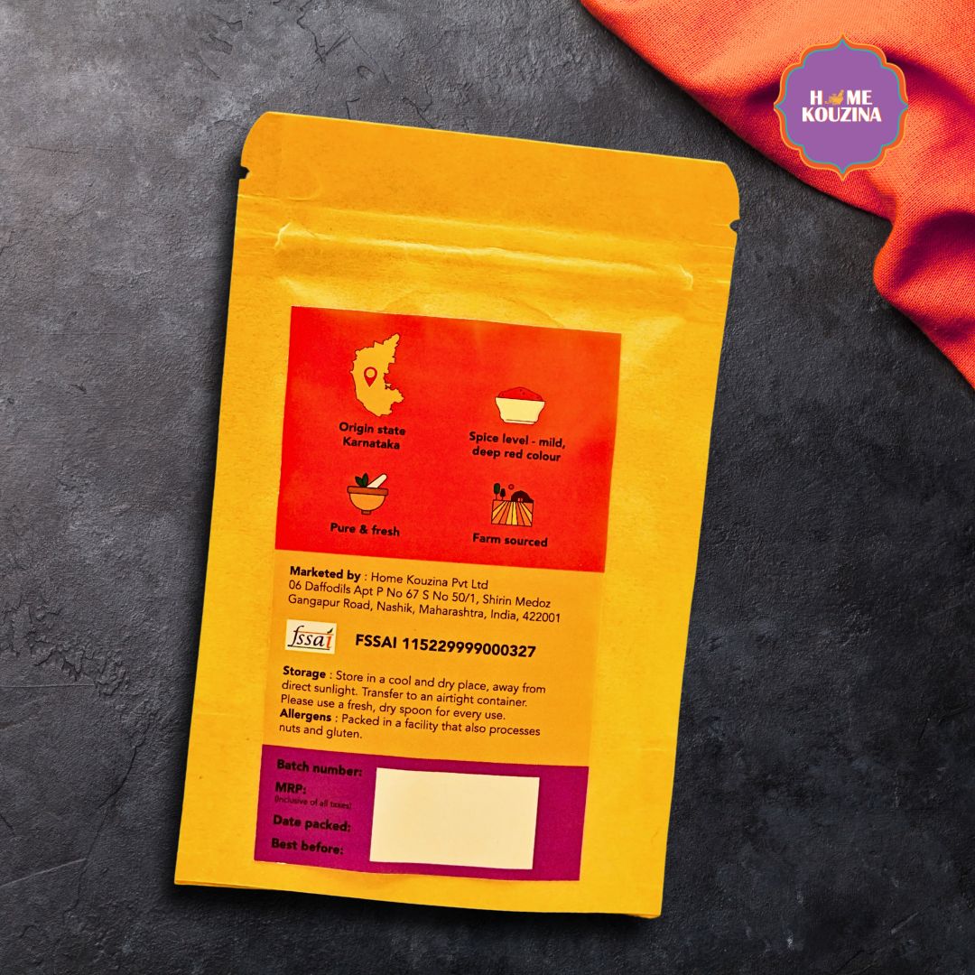 Back view of Home Kouzina Byadgi Chilli Powder 100g pack on grey table – nutritional info, usage instructions, and preservative-free, slow-ground Indian chilli powder