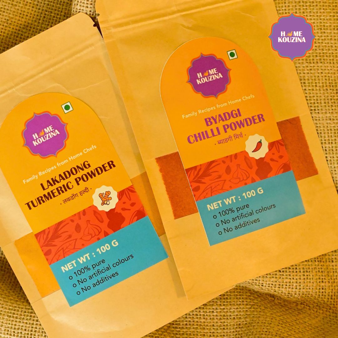 Top view of Home Kouzina Lakadong Turmeric Powder 100g and Byadgi Chilli Powder 100g packs on table – small-batch, all-natural Indian spices with vibrant color and aroma
