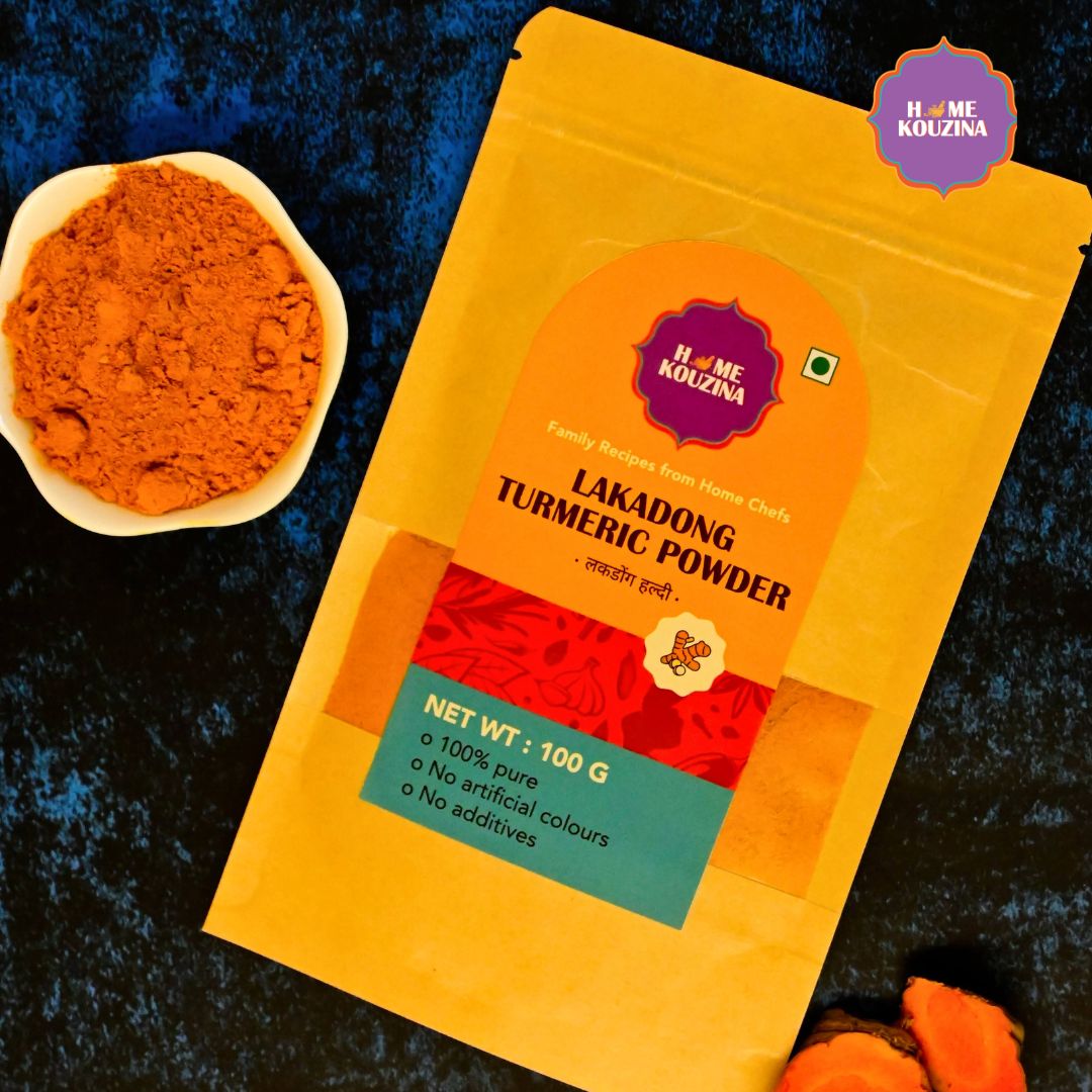 Top view of Home Kouzina Lakadong Turmeric Powder 100g Pouch and in abowl on blue table – naturally golden, aromatic, and anti-inflammatory Indian spice