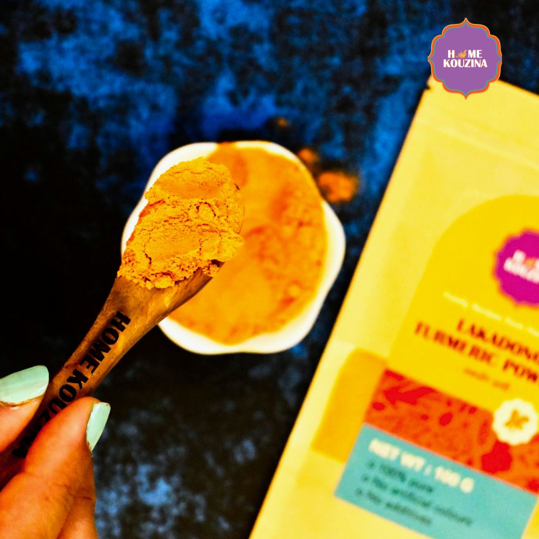 Top view of Home Kouzina Lakadong Turmeric Powder in a wooden spoon on blue table – naturally golden, aromatic, and anti-inflammatory Indian spice