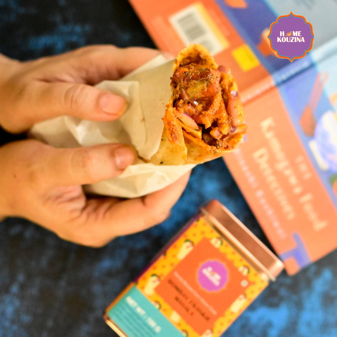 Top view of Home Kouzina Bombay Frankie Masala 150g tin with freshly made frankie held in hand – bold, tangy, and mildly spicy street-style spice blend for Mumbai frankies