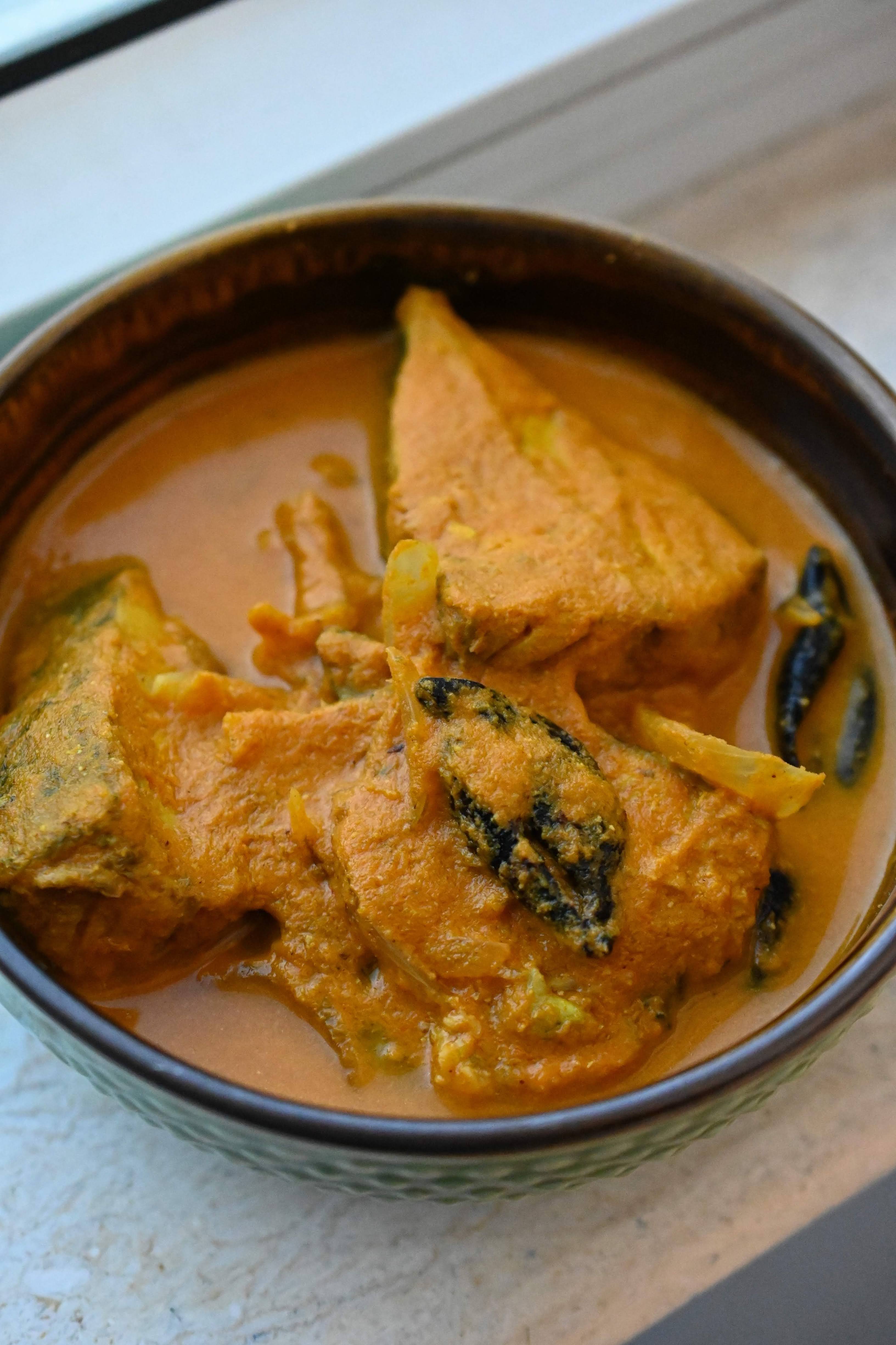 Top view of a rich, vibrant Goan fish curry in a bowl, garnished with coriander and paired with a side of steamed rice for a homely touch