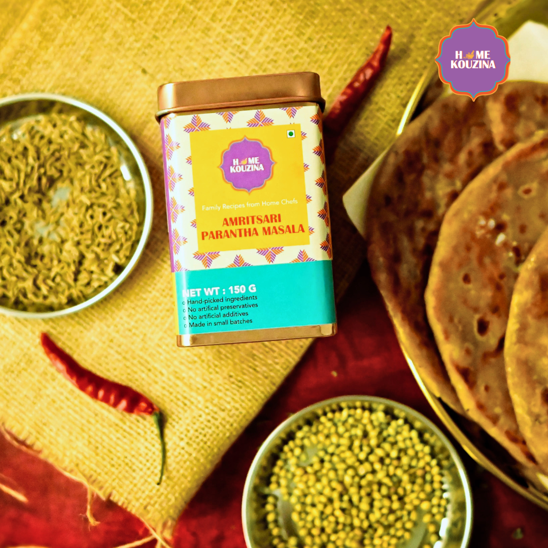 Top view of Home Kouzina Amritsari Parantha Masala 150g tin with freshly cooked paranthas on table and bowl of whole red chillies and mung beans – authentic North Indian spice blend