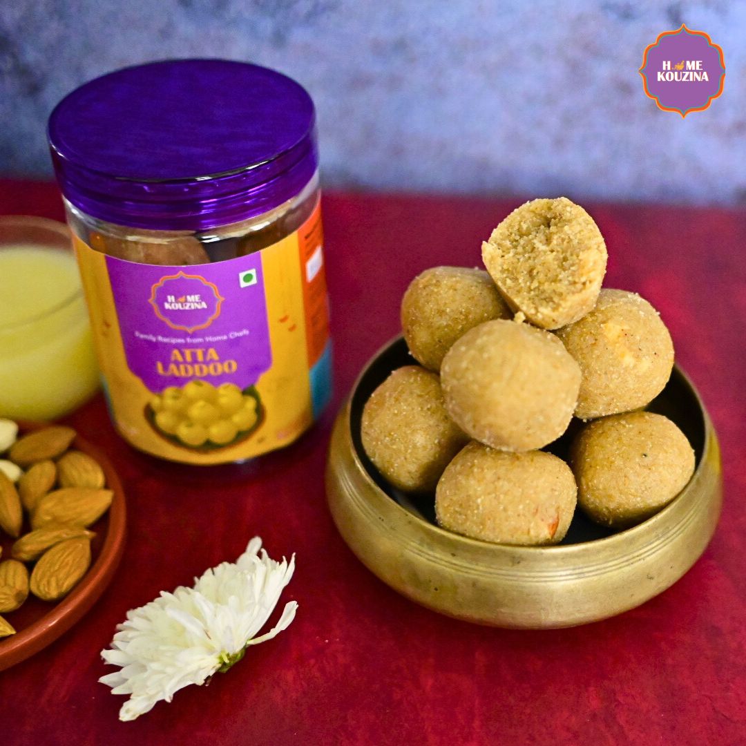 Home Kouzina's Atta Laddoo jar next to a brass bowl which has atta laddoos stacked on top of each other
