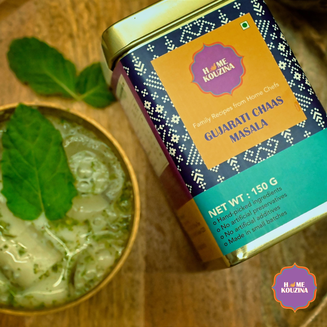 Top view of Home Kouzina Gujarati Chaas Masala 150g tin with chilled buttermilk in a glass garnished with mint – traditional Indian summer refresher drink