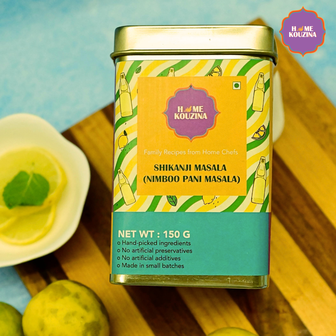 Close-up of Home Kouzina Shikanji Masala 150g tin pack on a table with lemons – tangy and spiced masala for traditional Indian nimbu paani with twist