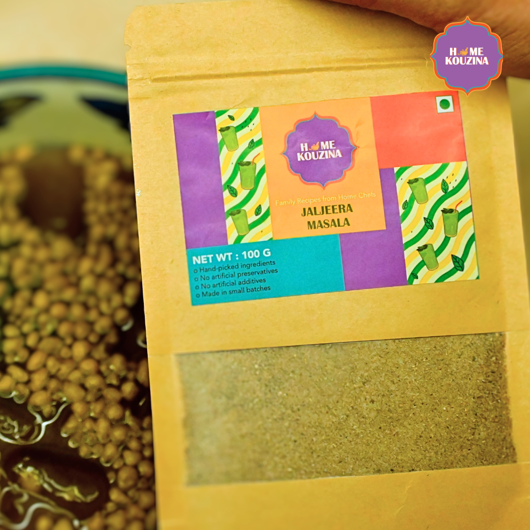 Home Kouzina Jaljeera Masala 100g pouch placed on table next to glass of jaljeera – traditional Indian drink masala
