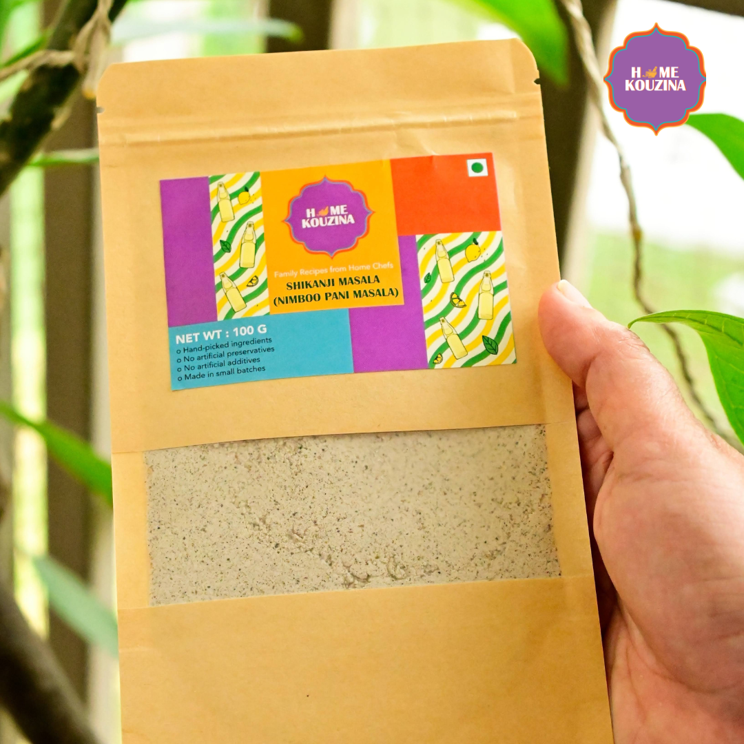 Hand holding Home Kouzina Shikanji Masala 100g pouch outdoors – small-batch, all-natural masala for flavorful shikanji