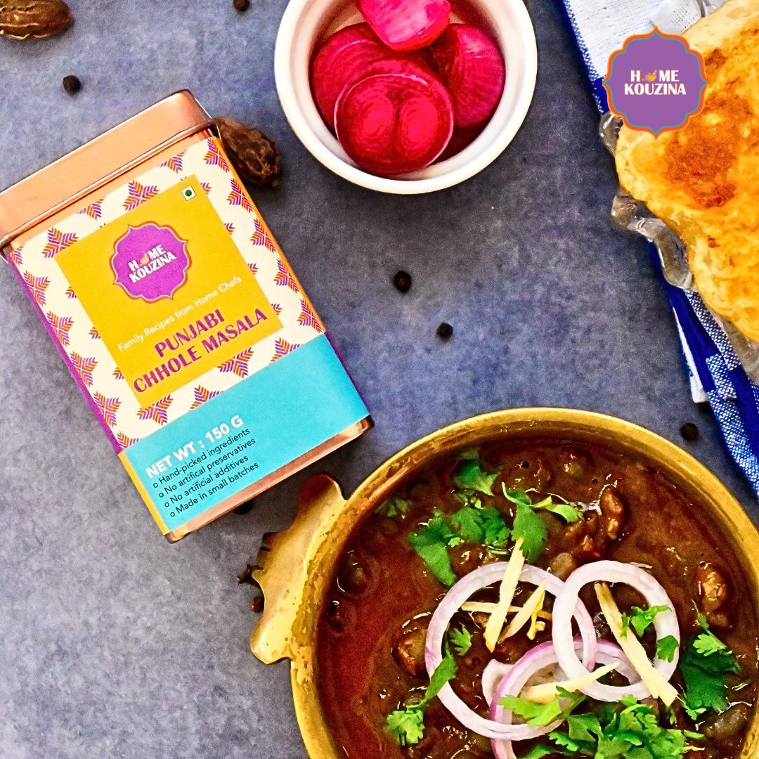 Top view of Home Kouzina Punjabi Chhole Masala 150g tin with bowl of rich, saucy Punjabi chhole garnished with onion and coriander, with a bowl of pickled red onions – traditional North Indian curry spice