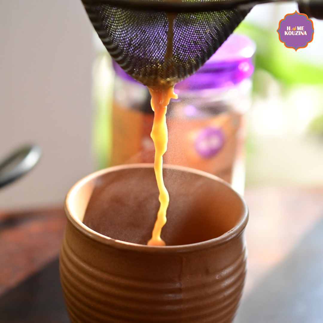 Chai tea being poured from a strainer into a brown ceramic cup with a blurred background.