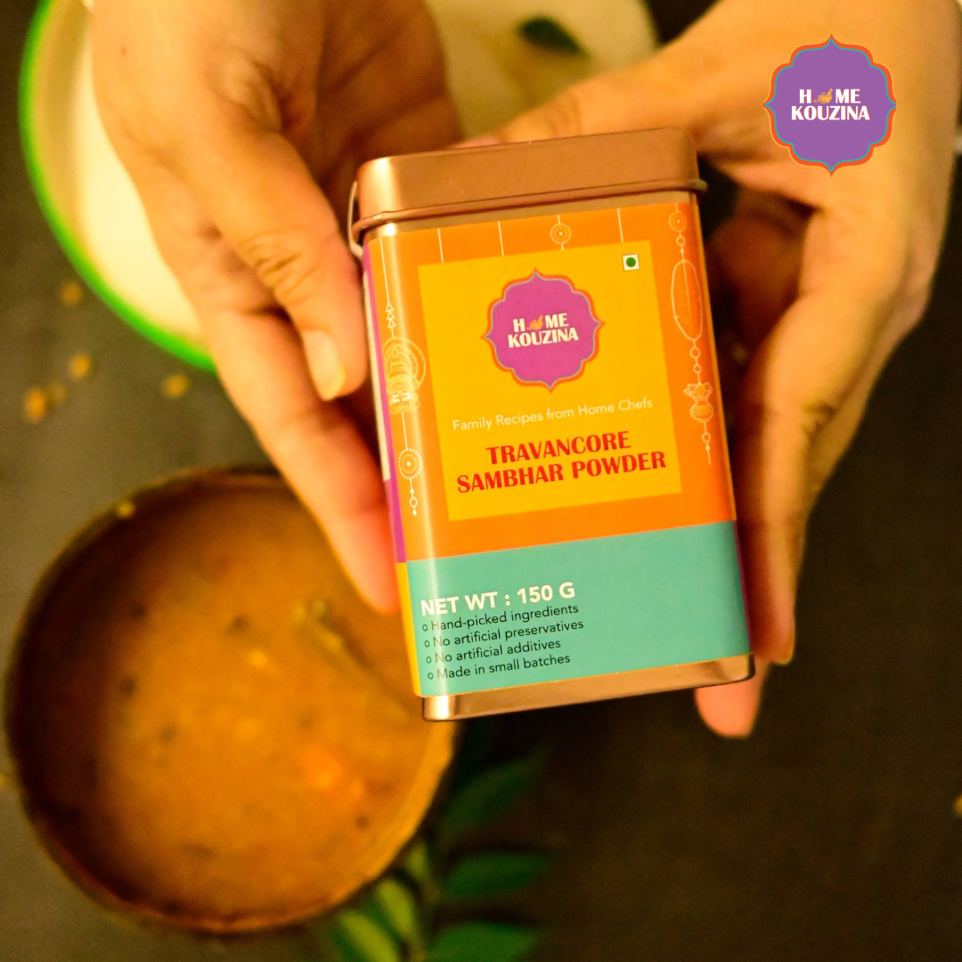 Top view of Home Kouzina Travancore Sambhar Powder 150g tin held on table with bowl of freshly made sambhar below – aromatic, bold, and comforting Kerala-style spice blend