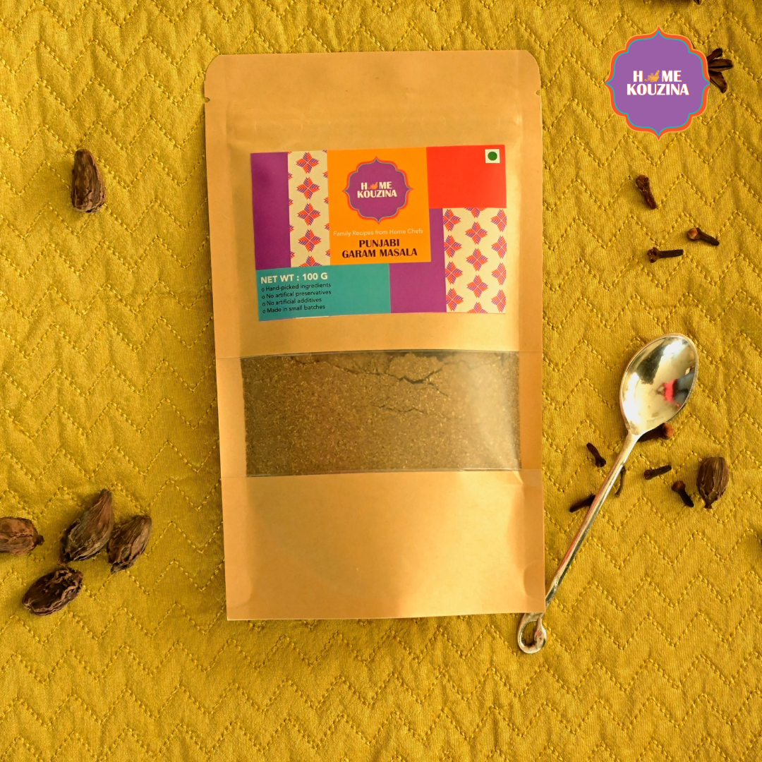 Top view of Home Kouzina Punjabi Garam Masala 100g pouch on table surrounded by whole spices and spoon – preservative-free, authentic Punjabi masala