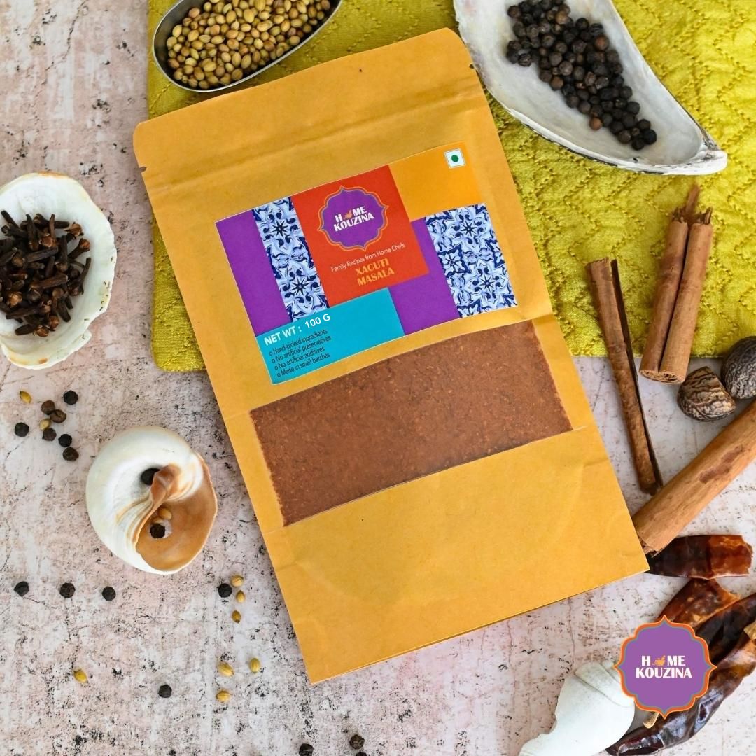 Top view of 100g Goan Xacuti Masala pouch on a table with scattered whole spices to evoke traditional Goan cooking