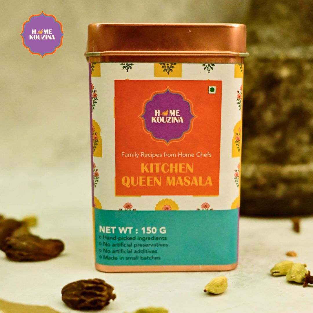 Home Kouzina Kitchen Queen Masala tin pack with mortar and pestle in the background and whole spices on a kitchen counter – aromatic all-in-one spice blend for home cooks
