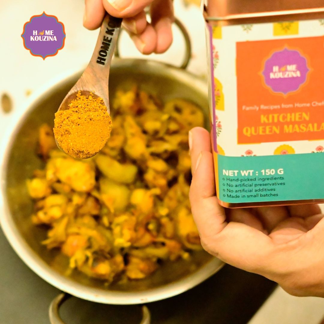 Top view of holding Home Kouzina Kitchen Queen Masala tin pack, and Home Kouzina spoon sprinkling masala into a bowl of cooked dal and sabzi