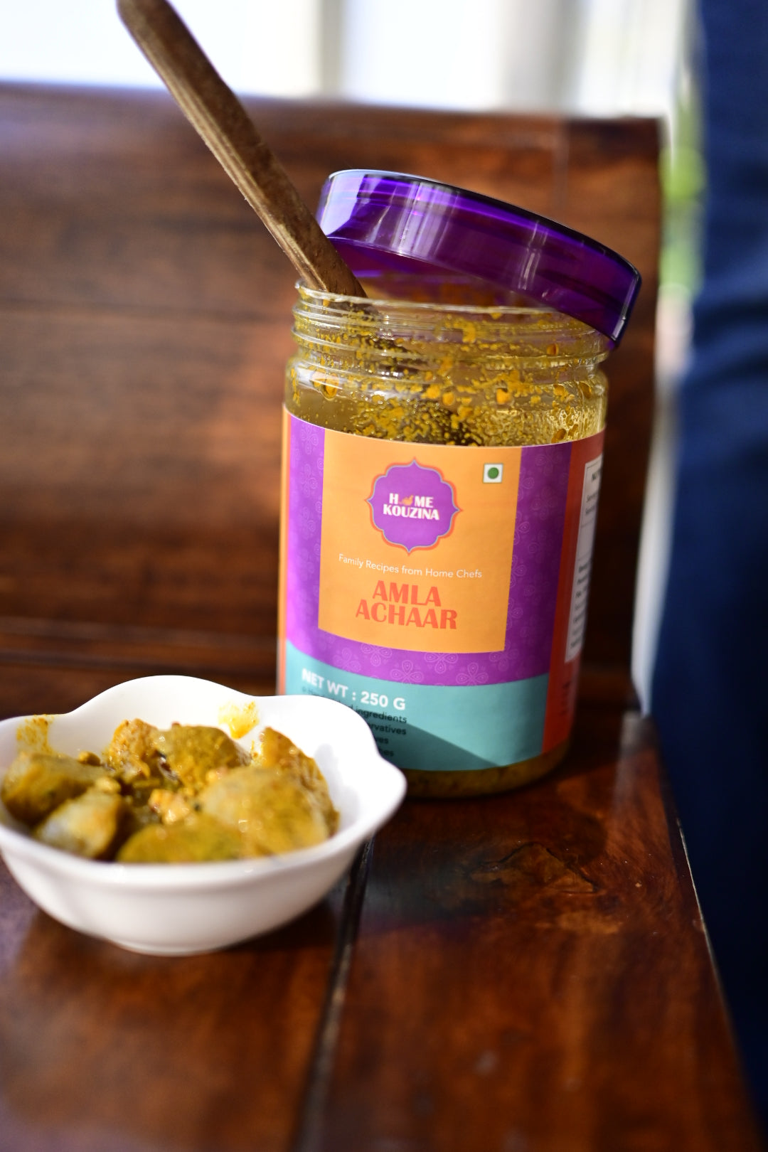 Bottle of Amala Achar with a spoonful of pickles on a wooden surface