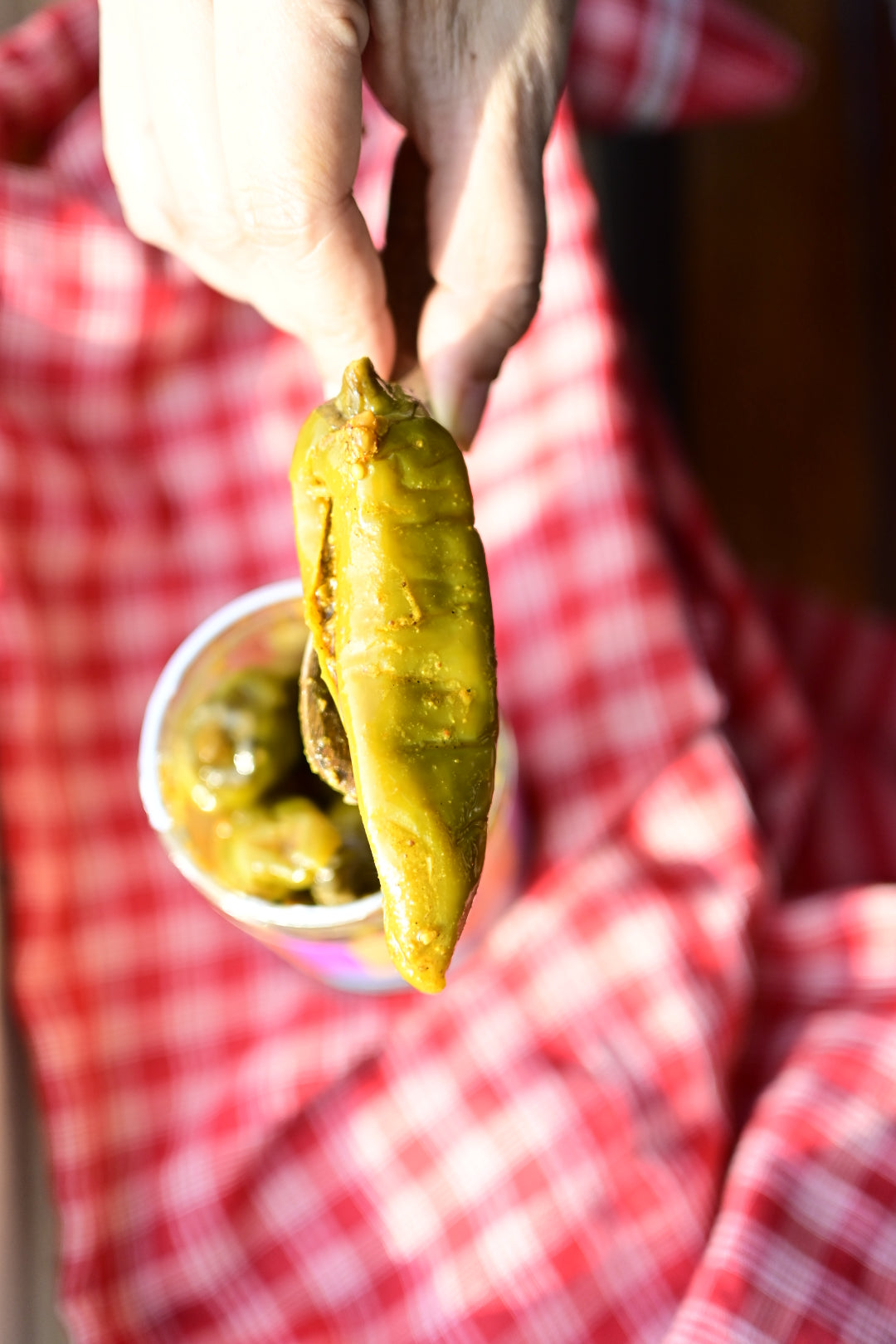 Person holding a green chili achaarpickle with a red checkered cloth in the background