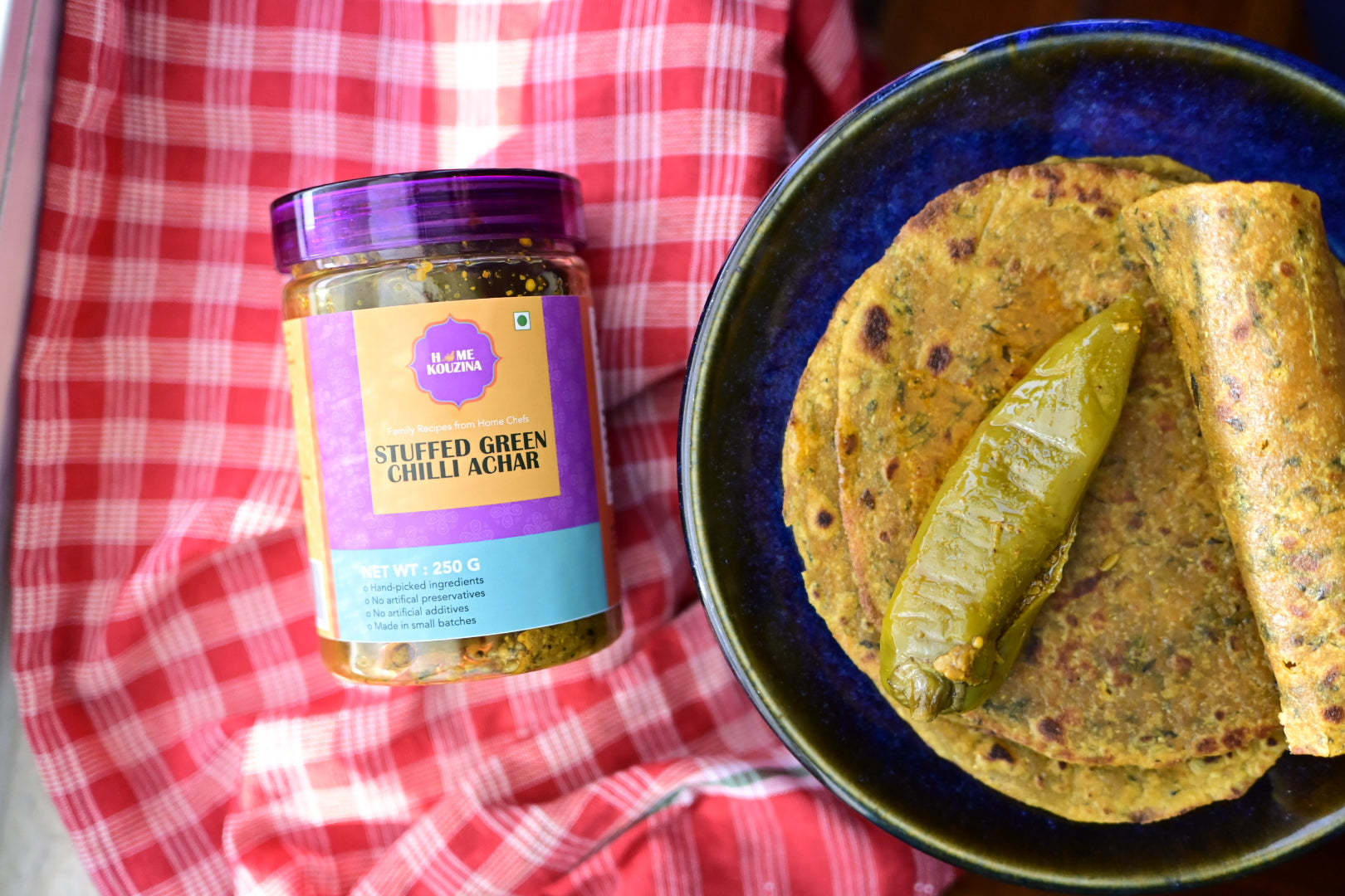 Jar of stuffed green chili achar with thepla on a checkered cloth