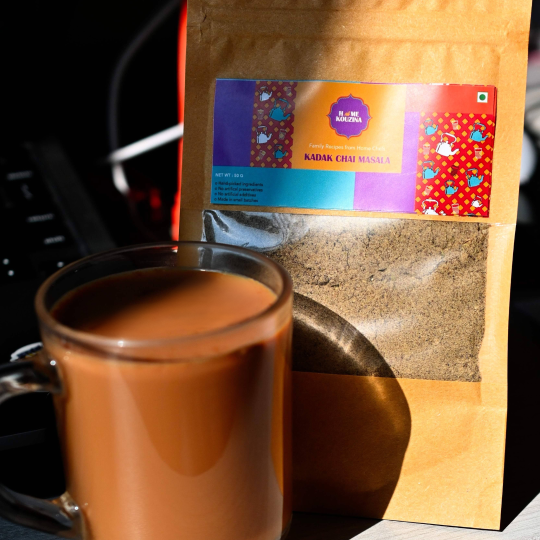A package of Kadak Chai Masala Spice Mix by Home kouzina , displayed on a wooden surface with a label showcasing the product name and a cup of chai 