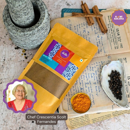 Top view of 100g Goan Roast Masala pouch on a rustic table with scattered whole spices to evoke traditional Goan cooking